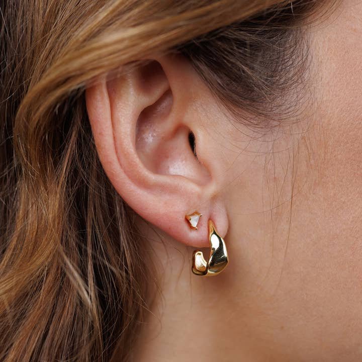 Close-up of a person's ear wearing Small Ripple Gold Hoop Earrings by JaxKelly—hypoallergenic, tarnish-free jewelry.