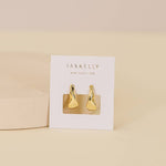 The Small Ripple Gold Hoop Earrings by JaxKelly are shown on a white JaxKelly card against a neutral background, highlighting these hypoallergenic and tarnish-free gold hoops.