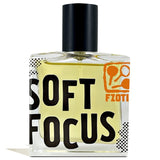 A rectangular glass perfume bottle with yellow liquid, black cap, and bold black "SOFT FOCUS" text. This summer scent from Fzotic features an orange logo and “Fzotic” in the top right corner.