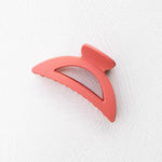 The Solid Matte Dix Cup Hair Clip by Tiepology, a curved 4-inch matte pink acrylic claw, rests on a white textured surface.