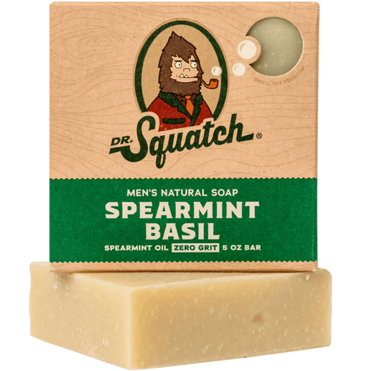 A box of Dr.Squatch Spearmint Basil Soap sits atop an unwrapped minted bar, featuring green and brown packaging with a cartoon mascot to invigorate your senses.