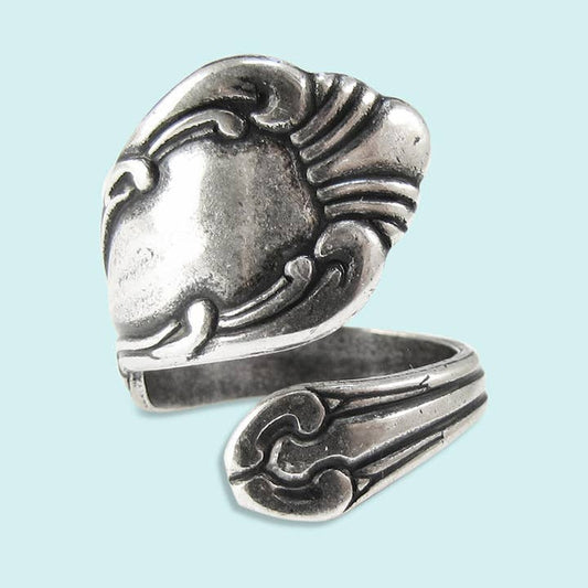 The Spoon Ring by Ornamental Things is crafted from sterling silver plate with ornate engraved details and is shaped like a spoon handle, displayed on a light blue background.