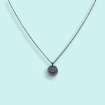 The Sterling Silver Evil Eye Medallion Necklace by Ornamental Things features a circular pendant with an engraved eye, shown on a light blue background.