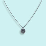 The Sterling Silver Evil Eye Medallion Necklace by Ornamental Things features a circular pendant with an engraved eye design, displayed on a light blue background.