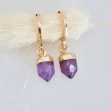 Mesa Blue’s Stone Bullet Amethyst Huggie Earrings feature 18K gold plated hoops with purple amethyst pendants capped in gold, shown against a light background.