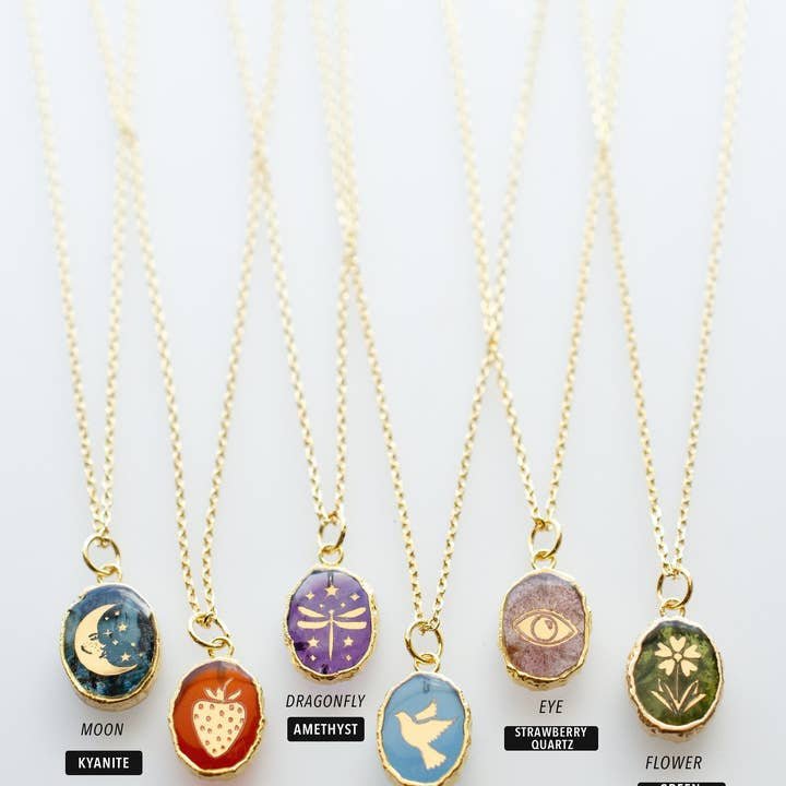 Six gold plated Stone Symbol Necklaces by Jill Makes feature diamond cut chains and oval natural stone pendants—moon, strawberry, dragonfly, bird, eye, and flower—with gemstone names labeled below.
