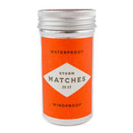 A metal container with an orange label reads "Storm Matches | Mollyjogger, 20 ct, waterproof and windproof matches.