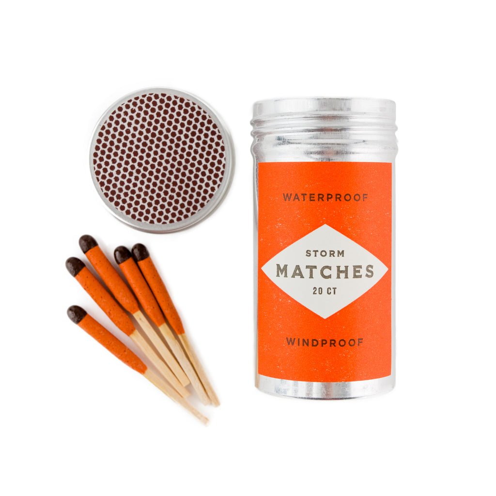 A metal container labeled "Mollyjogger Storm Matches" with a separate round striker and five orange-tipped, windproof matches from Mollyjogger displayed beside it.
