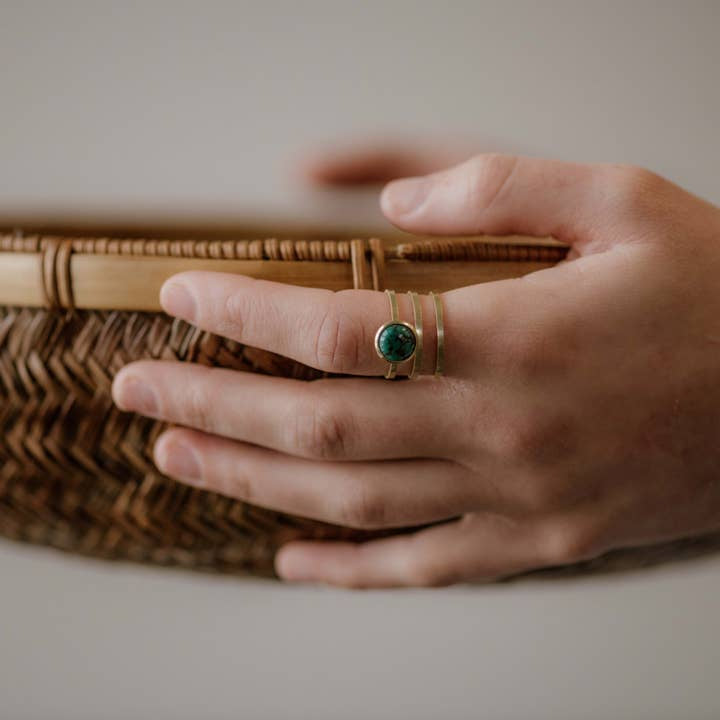 A hand wearing the Strata Ring Turquoise by CommonForm, featuring a bezel set turquoise stone, holds the edge of a woven basket.