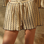 A person wears Promesa USA’s Striped Textured Knit Drawstring Shorts, featuring black vertical wavy stripes and a relaxed fit, styled with a black crop top.