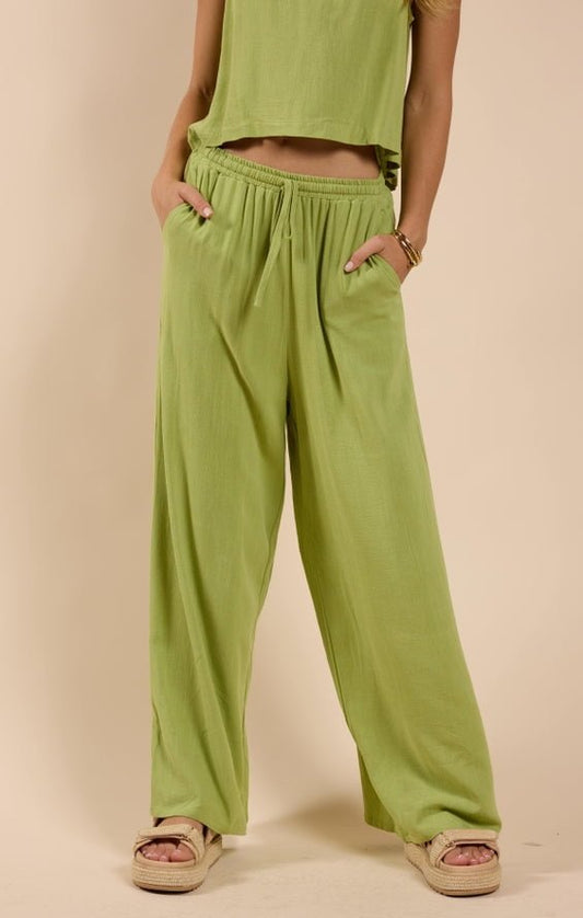 A person wears Sadie And Sage’s Sugarloaf Elastic Waist Pants in light green with a matching top, hands in pockets and facing forward, paired with beige platform sandals.