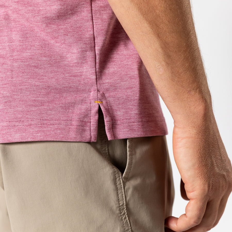A person wearing the Duck Head Summerford Performance Pique Polo in heathered pink and beige pants, with their right arm relaxed by their side.