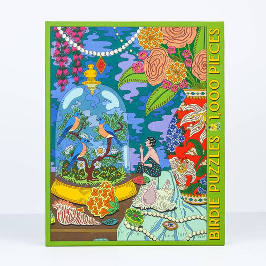 The Sunday Morning 1,000 Pieces jigsaw puzzle by Birdie Puzzles features vibrant artwork of birds in a glass dome, a seated figure, flowers, shells, and pearls—all crafted from recycled materials.