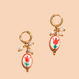 The Sweet Tulip Hoop by Peter and June features gold-plated waterproof hoops with red tulip charms and small white bead accents, displayed on a beige background.
