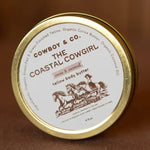 A round tin labeled "COASTAL COWGIRL | Cocoa and Coconut Tallow Body Butter" by Cowboy & Co. features a horse motif on the lid and contains a hydrating blend of grass-fed tallow, cocoa, and coconut for deeply nourished skin.