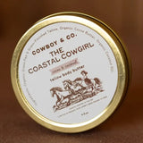 A round tin labeled "Cowboy & Co. Cocoa and Coconut Tallow Hydrating Body Butter," with art of two running horses, contains whipped body butter made with grass-fed tallow, suitable for sensitive skin.