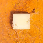 A bar of Health y Sol Tallow Soap with all-natural ingredients rests on orange-tinted water, surrounded by bubbles and ripples.