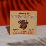 A box of Tallow Soap | Health y Sol sits on a white surface with an orange background. The packaging shows it’s fragrance free, made with all natural ingredients, and ideal for reducing acne or soothing eczema.