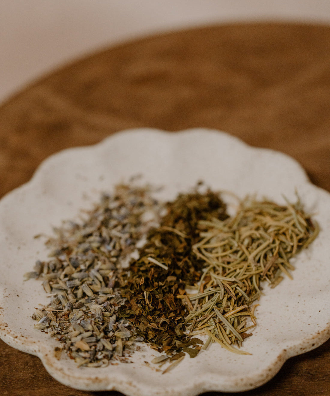 TAMED MANE | Rosemary Hair & Scalp Elixir by Cowboy & Co. sits on a white ceramic plate with dried herbs on wood—a perfect inspiration for natural hair and scalp care.