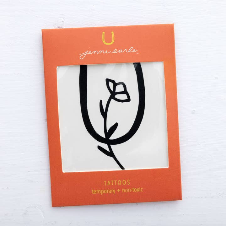 An orange package labeled "Jenni Earle" contains a non-toxic, long-lasting temporary tattoo from Jenni Earle, featuring a simple black line flower design.