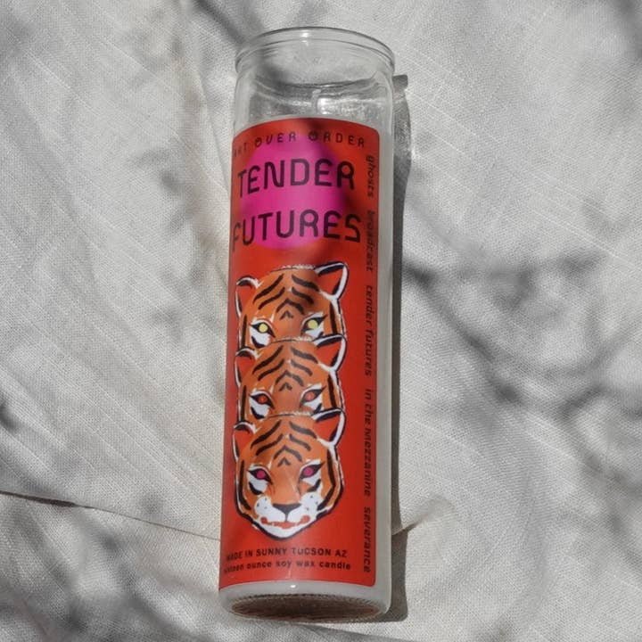 The Tender Futures Intention Candle by Art Over Order features a bright orange label with three illustrated tiger faces and "TENDER FUTURES," displayed on a white fabric background.