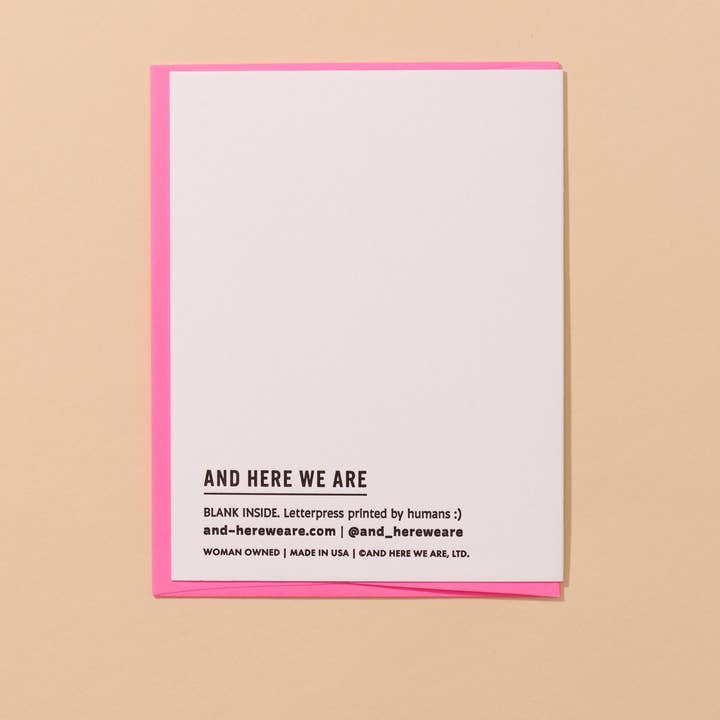 A white letterpress thank you card from And Here We Are, featuring a pink border, rests on beige. "AND HERE WE ARE" is printed at the bottom, with the product name "Thank Ye Kindly Ma'am | And Here We Are" and brand details below.
