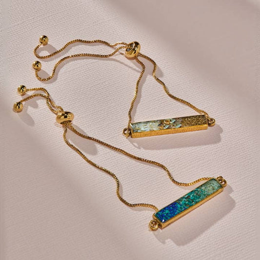 The Colorblock Ombre Adjustable Bracelet by cameoko features gold-plated, adjustable bands with rectangular multicolored inlay bars, creating a chic colorblock ombre effect. Displayed on a light pink textured surface.