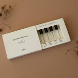 The Elsewhere Discovery Set by dilo includes five personal fragrance vial sprayers, arranged on a brown surface with dried plant stems.