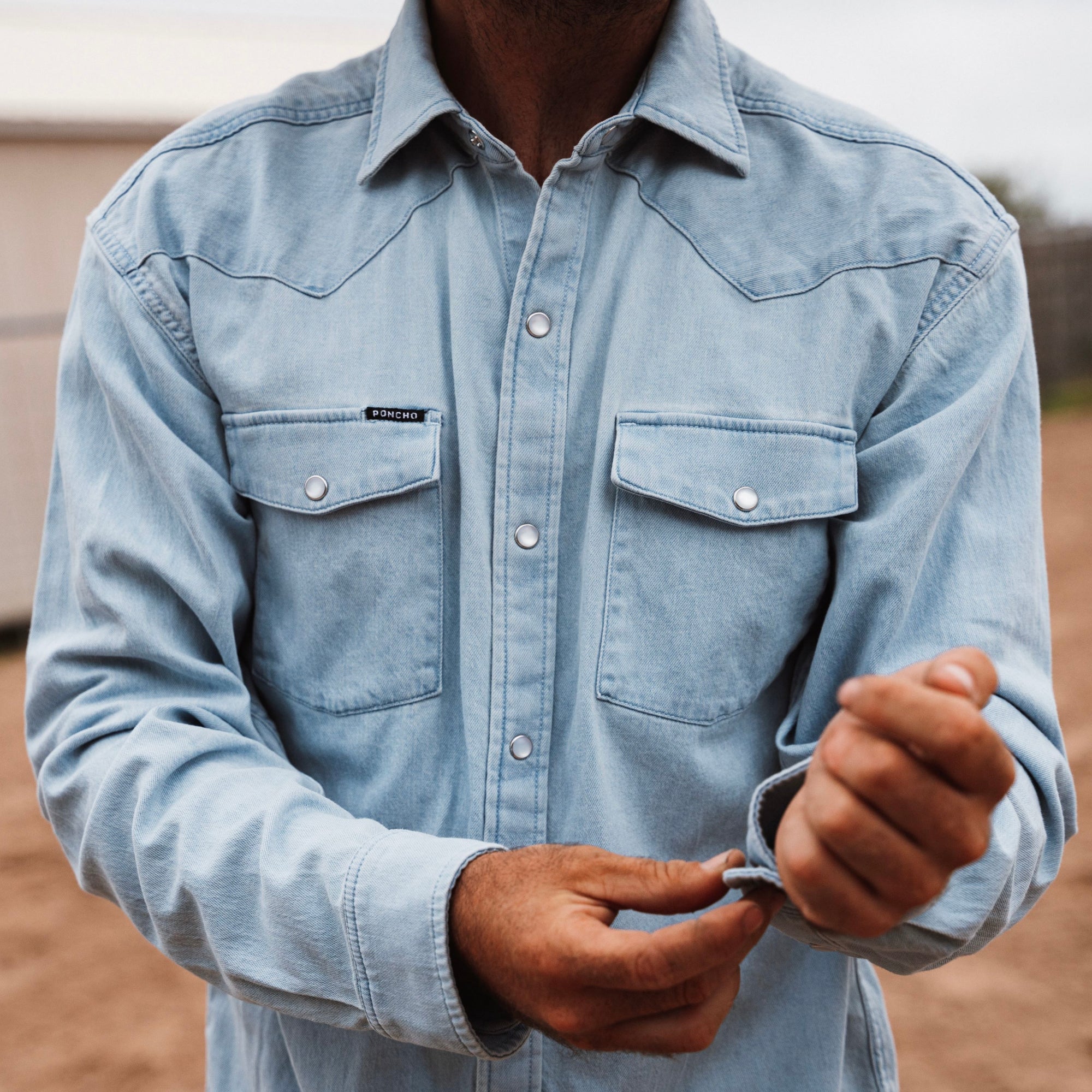 A person wearing The Marfa | Poncho by Poncho is buttoning the cuff of their sleeve outdoors.