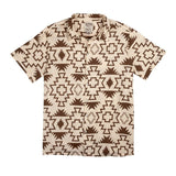 The Padre Shirt | Chama Chevron by Sendero Provisions Co. is a short-sleeved, button-up camp collar shirt featuring bold brown geometric patterns on a beige background.
