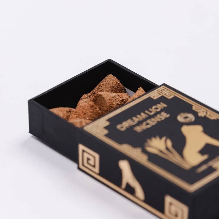 A black box labeled "The Wish Granter Incense | Dream Lion" from Dream Lion Incense, adorned with gold designs and partially open to show natural incense pieces inside, featuring scents such as copal and sandalwood.