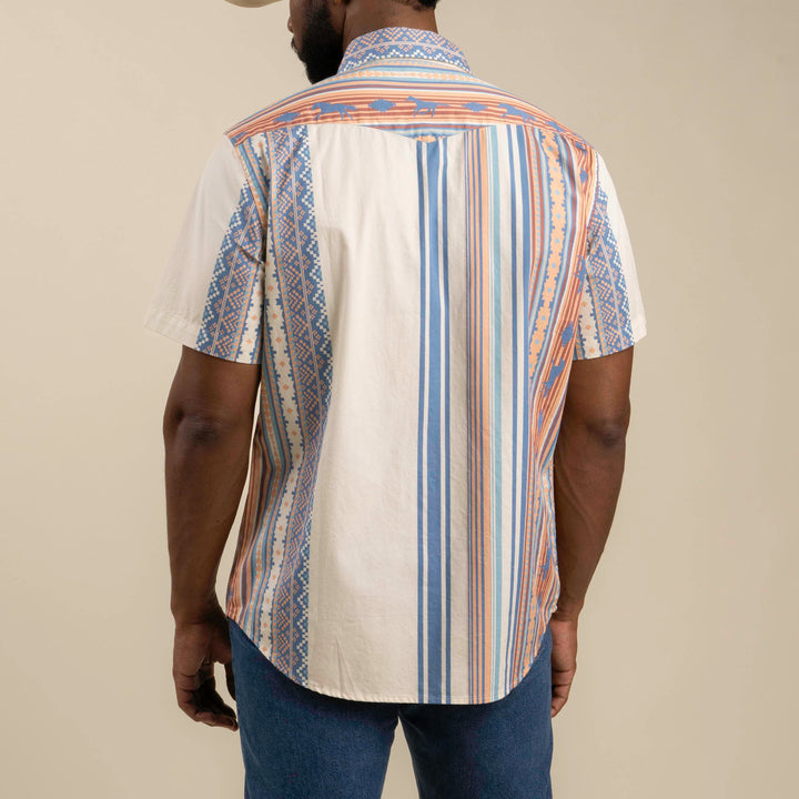 A person wearing The Wyatt Pearl Snap by Sendero Provisions Co.—a short-sleeve western shirt with blue, orange, and cream vertical patterns—viewed from the back and paired with blue jeans.