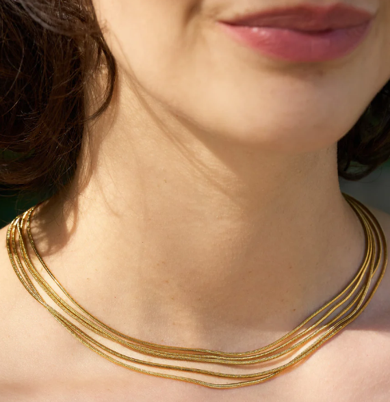 A woman shown from the neck up, lips and chin visible, wears the Thelma Layered Snake Chain necklace by Peter and June.