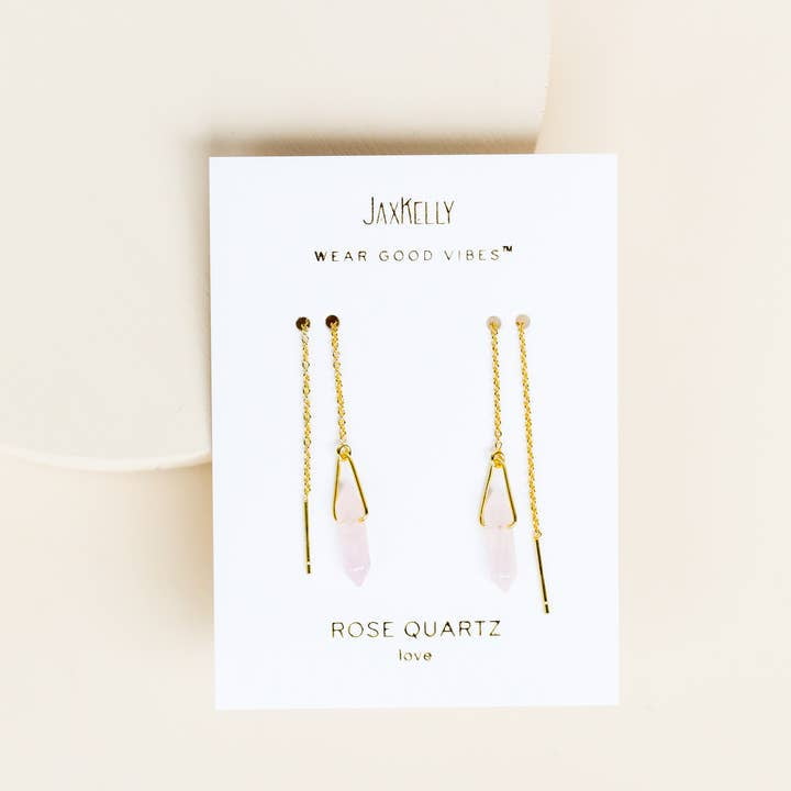 The JaxKelly Threader - Rose Quartz - Gold Earrings feature rose quartz crystals on gold threaders, displayed on a white card with "Wear Good Vibes" and "Rose Quartz love." These stylish earrings are perfect for those wanting hypoallergenic jewelry.