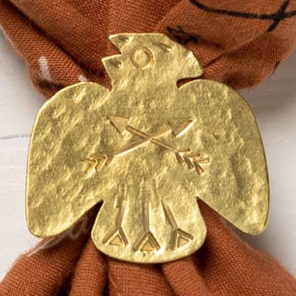 The Thunderbird Bandana Slide by Jenni Earle features a brass thunderbird holding arrows, fastened to brown patterned fabric for a bold western look.