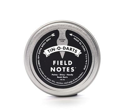 The Field Notes Tin-O-Darts is a round metal tin containing precision-cut steel Book Darts—sleek, reusable page markers ideal for marking your place in any book.
