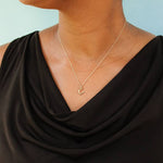 A person wearing a sleeveless black top and the Ornamental Things Tiny Gold Horseshoe Necklace, set against a light blue background.