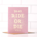 The "To My Ride Or Die" card by Daydream Prints features bold white lettering on pink, displayed on a brown envelope with a white tiled backdrop.