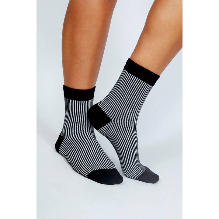 A person wearing Tailored Union Trey Ankle Socks—black and white vertical stripes, reinforced toe and heel, black cuffs—stands on a plain white background.
