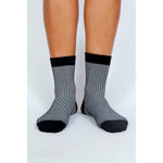 A person wearing Tailored Union Trey Ankle Socks—black and white vertically striped combed cotton with black toes, heels, and cuffs—stands on a white background.