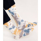 Person wearing Trippy Crew Socks by Tailored Union, featuring a colorful tie-dye design in blue, yellow, and gray, standing against a plain light background.