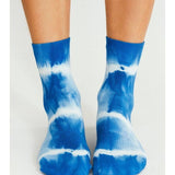 Wearing Tailored Union’s Trippy Tie Dye Ankle Sock-Blue, a pair of feet stand on a light surface, channeling fun festival vibes with their bold blue and white design.
