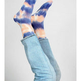 Two legs in blue jeans are raised, displaying Tailored Union’s Trippy Tie Dye Ankle Sock in Pink against a plain background.