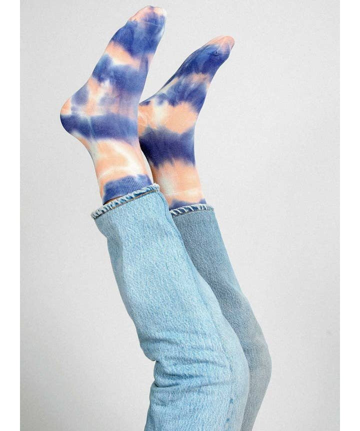 Two legs in blue jeans are raised, displaying Tailored Union’s Trippy Tie Dye Ankle Sock in Pink against a plain background.