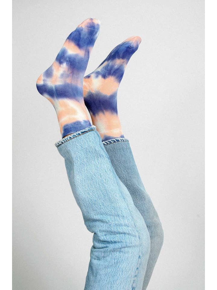 Two legs in blue jeans are raised, displaying Tailored Union’s Trippy Tie Dye Ankle Sock in Pink against a plain background.