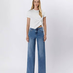 A woman faces forward in a white short-sleeve twisted t-shirt, silver open-toe heels, and Vervet's Tummy Control Super High Rise Baggy Wide Jeans against a plain white background.