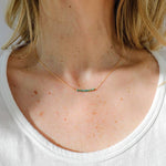 Close-up of a woman's neck wearing the Turquoise Bead Necklace by Ornamental Things, featuring an adjustable gold-filled chain with a row of small turquoise beads, styled with a white shirt.