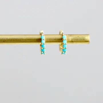 The Turquoise Huggie Earrings by Mesa Blue are shown hanging on a horizontal brass rod against a plain light background.