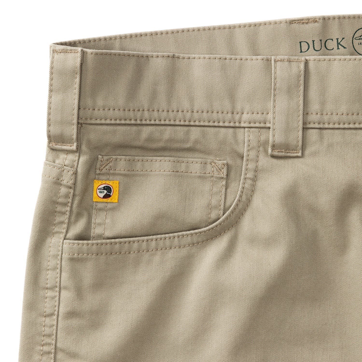 Close-up of the front pocket area of Duck Head’s Twill 5 Pocket Briar Pant, highlighting relaxed fit tan stretch twill fabric, stitching details, belt loops, and a small yellow tag on the coin pocket.