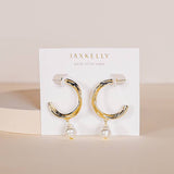 The Twisted Pearl Drop Hoop - Gold Earrings by JaxKelly feature gold-toned twisted hoops with dangling freshwater pearls, presented on a branded card. Hypoallergenic and perfect for sensitive ears.